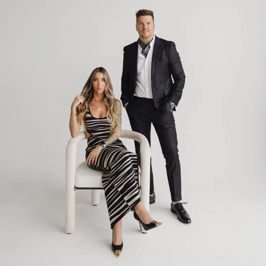A stylish couple dressed in elegant black and white outfits posing against a light background.